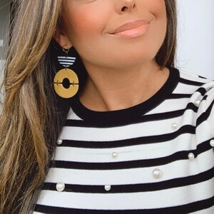 Könnte beinhalten: Eine Frau trägt ein schwarz-weiß gestreiftes Shirt mit Perlenbesatz. Sie trägt große geometrische Ohrringe in Gold und Schwarz.