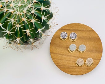 May include: A set of six earrings with a geometric pattern in black and white. The earrings are made of polymer clay and have a gold fringe. The earrings are displayed on a wooden surface.