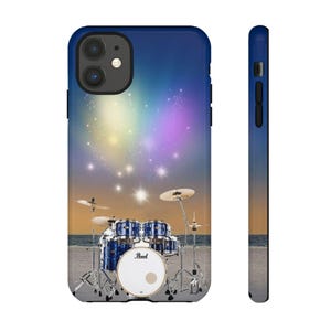 Op de afbeelding: Een blauwe telefoonhoes met een drumstel op een strand onder een sterrenhemel. De drumkit heeft blauwe en witte accenten, met bekkens en een grote trommel. De achtergrond loopt over van oranje naar blauw.
