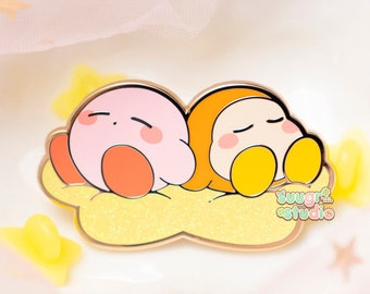 May include: A pink and orange cartoon character pin with a yellow star design. The characters are sleeping on a yellow cloud with a gold outline. The pin says "Sugar Studio" in the bottom right corner.