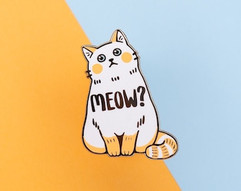 May include: White enamel pin with a cartoon cat with orange ears and a tail. The cat is sitting with its paws together and has a surprised expression. The text "MEOW?" is printed on the cat's chest.