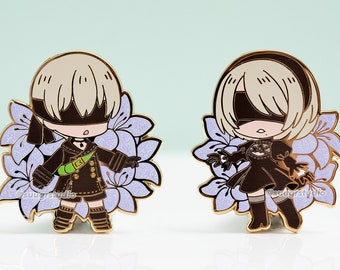 May include: Two gold-colored enamel pins featuring characters from the video game Nier Automata. The pins are set against a light blue background. The characters are depicted in a chibi style, with large heads and small bodies. The first pin features a character with short, blonde hair and a black blindfold. The character is wearing a black and green outfit and is surrounded by purple flowers. The second pin features a character with long, blonde hair and a black blindfold. The character is wearing a black dress and is surrounded by purple flowers.