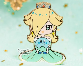 May include: A gold-colored enamel pin featuring a cartoon depiction of Princess Peach from the Super Mario franchise. She is wearing a green dress and a crown, and holding a blue Kirby character.