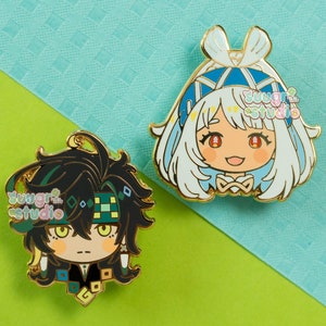 Pode incluir: Dois pinos de esmalte com desenhos de personagens de desenhos animados. Um pino apresenta um personagem com cabelo preto e olhos verdes, vestindo uma roupa preta e verde. O outro pino tem um personagem com cabelo branco e detalhes azuis. Ambos os pinos têm bordas douradas.