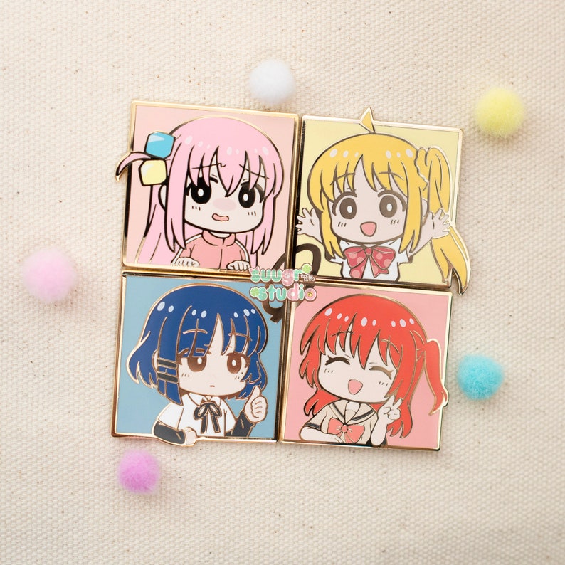 May include: Four square enamel pins featuring cartoon characters with different coloured hair and clothing. The characters are smiling and have large eyes. The pins are gold-coloured and have a glossy finish.