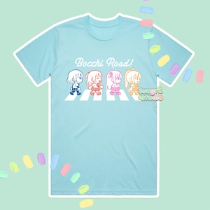 Può includere: Maglietta blu chiaro con una grafica bianca di quattro ragazze dei cartoni animati che attraversano un passaggio pedonale. Il testo "Bocchi Road!" è sopra le ragazze.