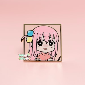 May include: A pink enamel pin featuring a cartoon character with pink hair, a pink shirt, and a surprised expression. The character is wearing a blue and yellow bow. The pin is set against a gold background.