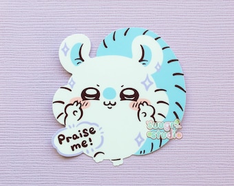 May include: A white and light blue sticker featuring a cartoon creature with a cute expression and the text "Praise me!". The sticker has a light purple background and the creature has blue accents and sparkles.