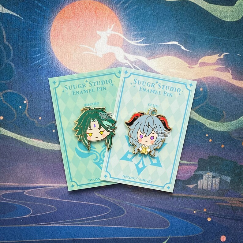 May include: Two enamel pins featuring anime characters. The pins are on cards with the text "SUUGR STUDIO. ENAMEL PIN" and the character's element. The left pin features a green-haired character with a purple gem on their forehead. The right pin features a blue-haired character with a red horn and a bell around their neck.