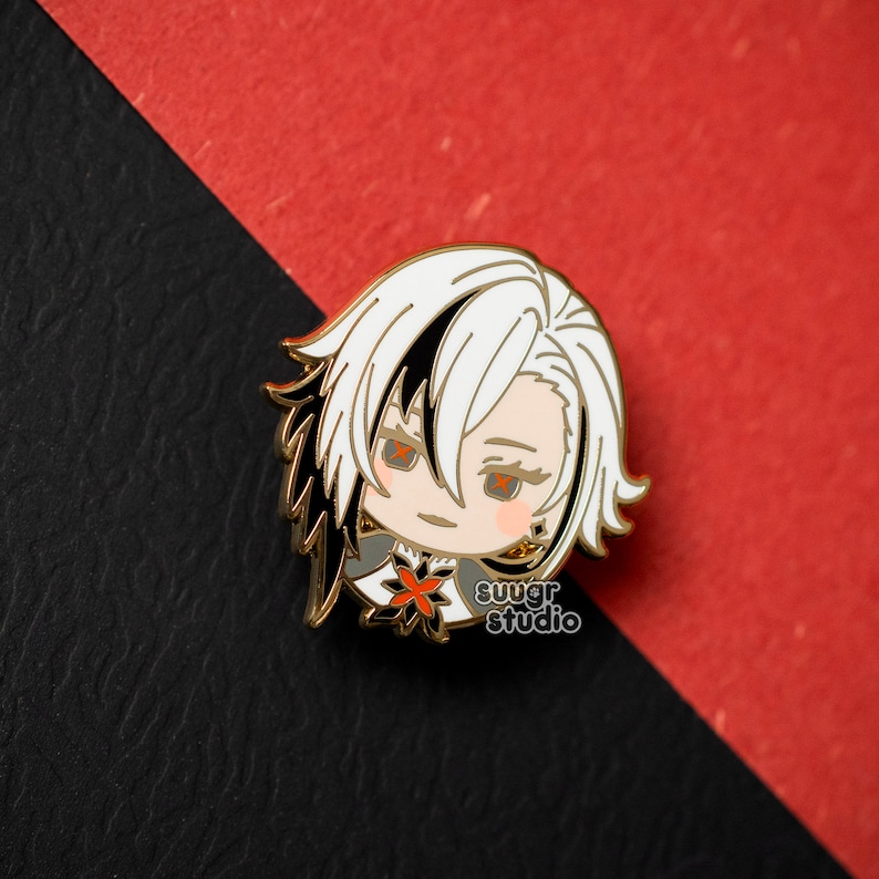 May include: Gold-colored enamel pin featuring a cartoon character with white hair, black eyes, and a red flower on their chest. The character is wearing a black and white outfit. The pin has the text "sugar studio" on the bottom.