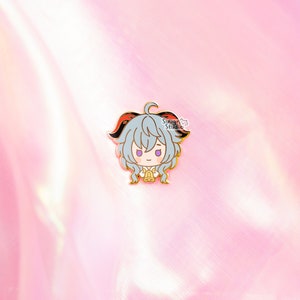 May include: A gold-colored enamel pin featuring a cartoon character with gray hair, red horns, and a white shirt. The character is holding a bell in their hands. The pin has a white background with the text "Sough Studio" in black.
