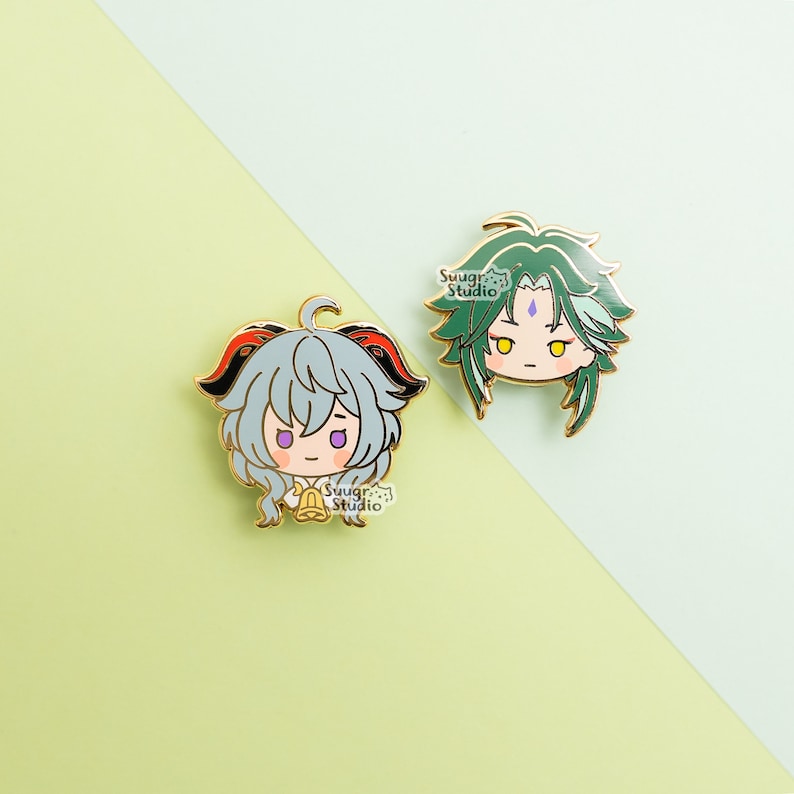 May include: Two enamel pins featuring anime characters. The first pin is green and features a character with green hair and a purple gem on their forehead. The second pin is a light blue character with red and black horns and a gold bell. Both pins have the text "Swagr Studio" on them.