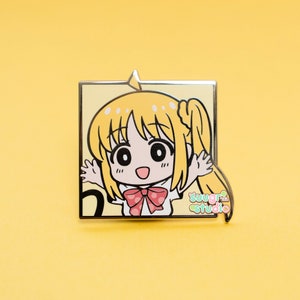 May include: A yellow and white enamel pin featuring a cartoon character with blonde hair, a red and white polka dot bow, and the text "sugar studio".
