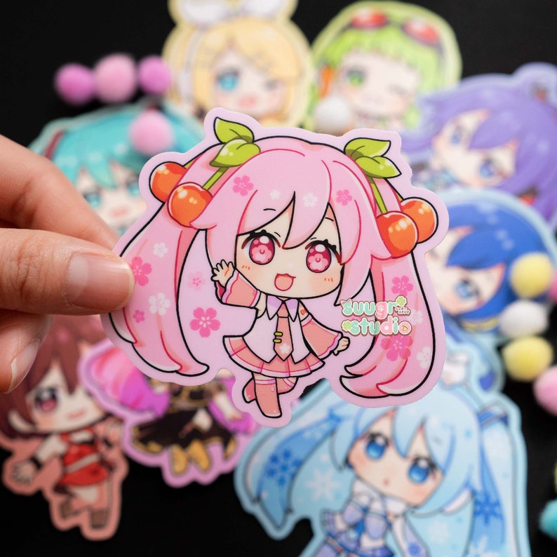 K&ouml;nnte beinhalten: Ein rosa Anime-Charakter-Aufkleber mit Kirschbl&uuml;ten und zwei Kirschen auf dem Kopf. Der Aufkleber hat den Text "sugar studio" unten.