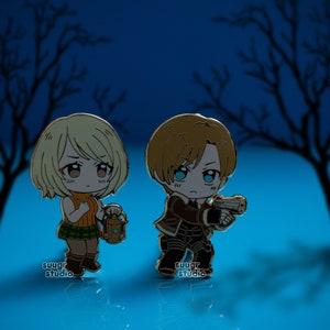 K&ouml;nnte beinhalten: Zwei goldfarbene Emaille-Pins, die Anime-Charaktere darstellen. Die weibliche Figur h&auml;lt eine Laterne und die m&auml;nnliche Figur h&auml;lt eine Pistole. Beide Figuren haben gro&szlig;e Augen und tragen Freizeitkleidung. Die Pins sind vor einem dunkelblauen Hintergrund mit einer Silhouette von B&auml;umen platziert.