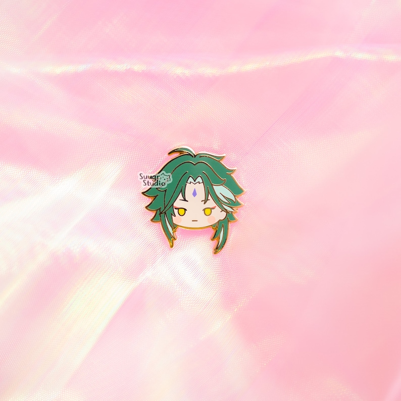 May include: A green and gold enamel pin featuring a cartoon character with green hair and a light blue gem on their forehead.