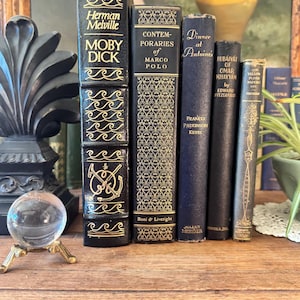 May include: A collection of five vintage hardcover books standing upright, including Moby Dick by Herman Melville, Contemporaries of Marco Polo, Dinner at Antoine's by Frances Parkinson Keyes, Rubaiyat of Omar Khayyam, and The Yellow Plush Papers.