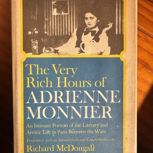 May include: A hardcover book titled The Very Rich Hours of Adrienne Monnier, An Intimate Portrait of the Literary and Artistic Life in Paris Between the Wars, translated by Richard McDougall, featuring a black and white photo of a person.