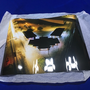 May include: An aerial view of a train station at night. The station has three buildings with a large, dark roof. The buildings are illuminated by bright lights. The train tracks are visible in the foreground.