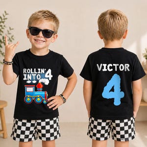 May include: A black short-sleeved t-shirt featuring a graphic of a blue train with the text Rollin' Into 4 on the front and the name Victor with a large blue number 4 on the back, paired with black and white checkered shorts.