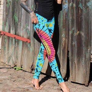 May include: A woman wearing a black tank top with a side cut-out and tie-dye leggings. The leggings are blue, green, yellow, pink, and orange.