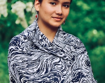 Könnte beinhalten: Eine Frau mit dunklen Haaren trägt einen weißen und schwarzen gemusterten Schal. Der Schal hat ein wirbelndes, marmoriertes Design. Sie trägt Ohrringe mit roten Steinen.
