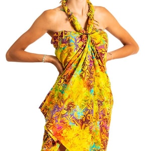 Op de afbeelding: Een gele, oranje en blauwe sarong met bloemenprint, gebonden tot een halterjurk.