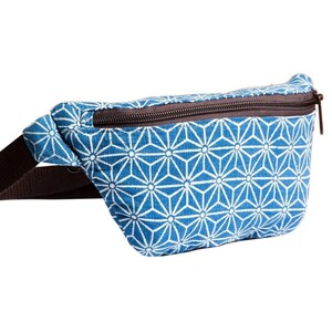 Pode incluir: Uma pochete azul e branca com padrão e uma alça ajustável marrom. A pochete tem um fecho de correr.