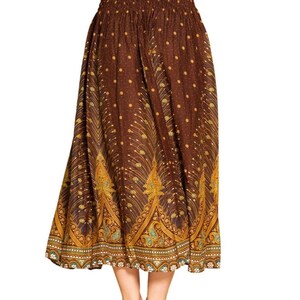 May include: A long, brown skirt with an elastic waistband and a flowing silhouette. The skirt features a repeating pattern of gold and teal peacock feather designs, with small gold dots scattered throughout the fabric.