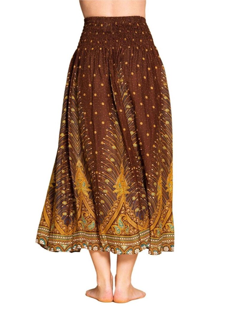 May include: A long, brown skirt with an elastic waistband and a flowing silhouette. The skirt features a repeating pattern of gold and teal peacock feather designs, with small gold dots scattered throughout the fabric.