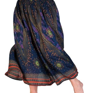 May include: A flowing, navy blue skirt with an elastic waistband and a vibrant, patterned design. The skirt features a repeating pattern of peacock-like motifs in shades of purple, green, and orange. The hemline is trimmed with a thin orange border.