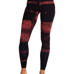 May include: Black leggings with a red tie-dye pattern. The leggings have a high waist and a form-fitting design. The red dye is arranged in horizontal bands across the legs, creating a unique visual effect. The fabric appears soft and comfortable.