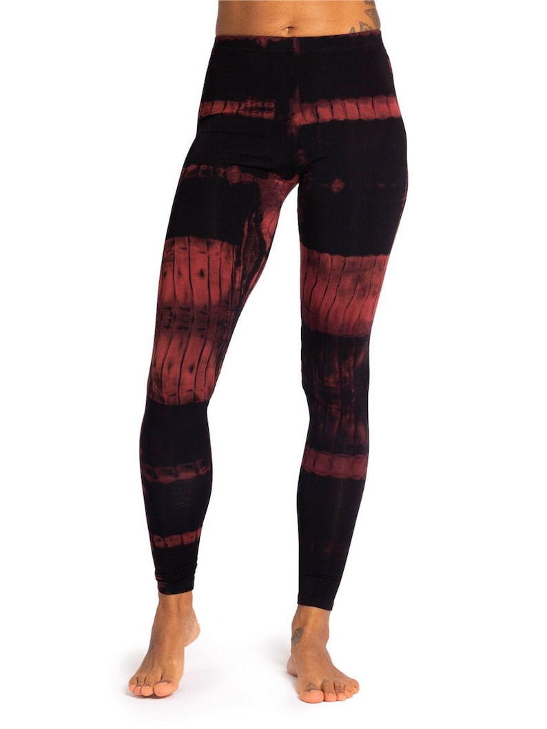 May include: Black leggings with a red tie-dye pattern. The leggings have a high waist and a form-fitting design. The red dye is arranged in horizontal bands across the legs, creating a unique visual effect. The fabric appears soft and comfortable.