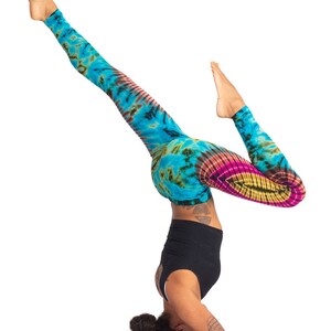 May include: A person in a blue, green, pink, and yellow tie-dye leggings is doing a headstand. They are wearing a black tank top and have their hair pulled back in a bun.