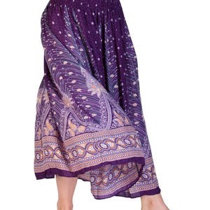 May include: Purple harem pants with an elastic waistband and a decorative paisley and floral border. The pants feature a flowing, wide-leg design and a patterned print in shades of purple, gold, and white. The fabric appears lightweight and suitable for warm weather.