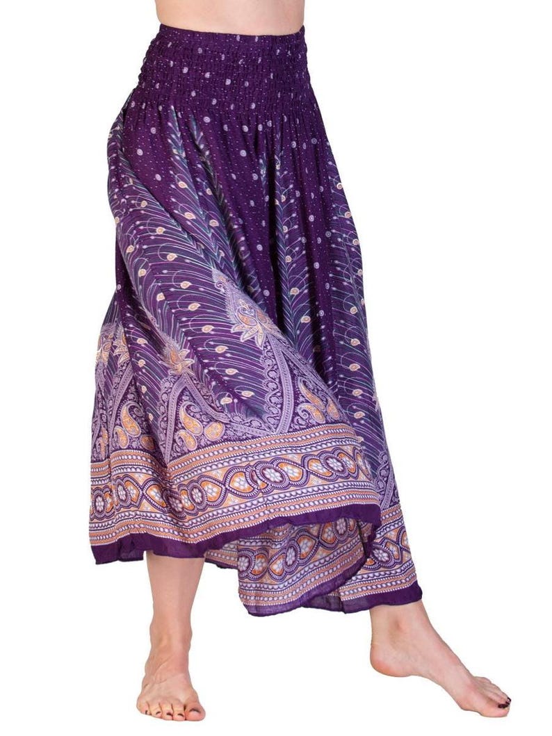 May include: Purple harem pants with an elastic waistband and a decorative paisley and floral border. The pants feature a flowing, wide-leg design and a patterned print in shades of purple, gold, and white. The fabric appears lightweight and suitable for warm weather.