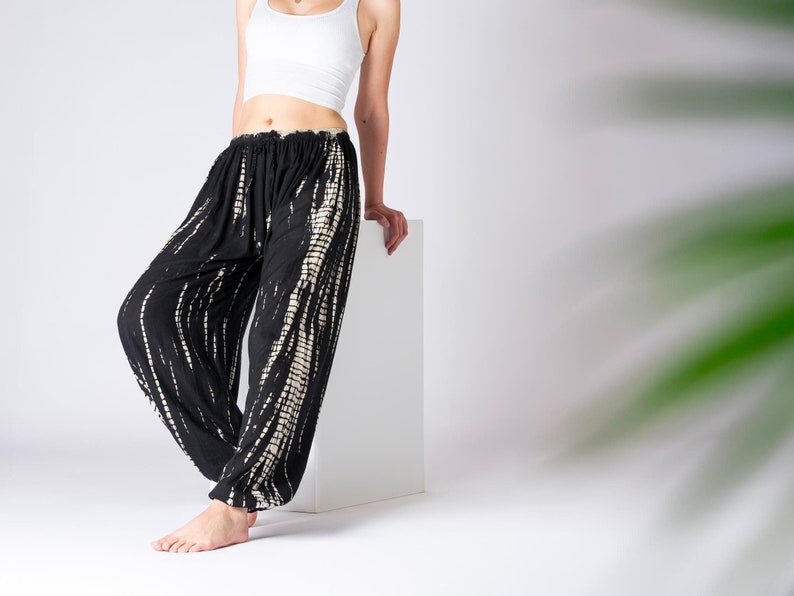 Locker geschnittene schwarze Haremshose mit beige vertikalen Tie-Dye-Streifen, elastischer Bund und Knöchelbündchen, getragen von Modell im weißen Crop-Top.