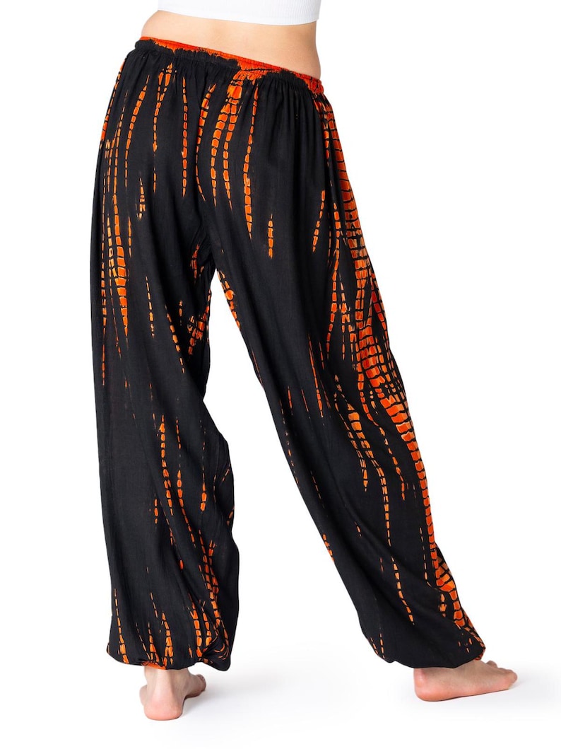 Locker geschnittene schwarze Chillhose mit vertikalem orangefarbenem Tie-Dye-Muster, elastischer Bund und Knöchelbündchen, Rückansicht.