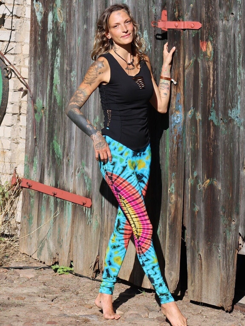 May include: A woman wearing a black tank top with a side cut-out and tie-dye leggings. The leggings are blue, green, yellow, pink, and orange.