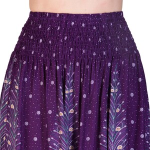 May include: A purple skirt with a smocked waistband and a flowing design. The skirt features a repeating pattern of peacock feather motifs and small white polka dots. The fabric has a rich, deep purple hue.