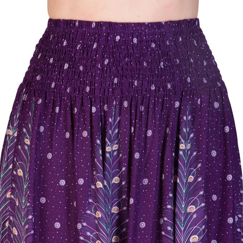 May include: A purple skirt with a smocked waistband and a flowing design. The skirt features a repeating pattern of peacock feather motifs and small white polka dots. The fabric has a rich, deep purple hue.