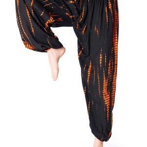 Schwarze Haremshose mit auffälligen orangefarbenen Tie-Dye-Streifen, elastischer Bund und Knöchelbündchen, Modell hebt ein Bein im Yoga-Stil.
