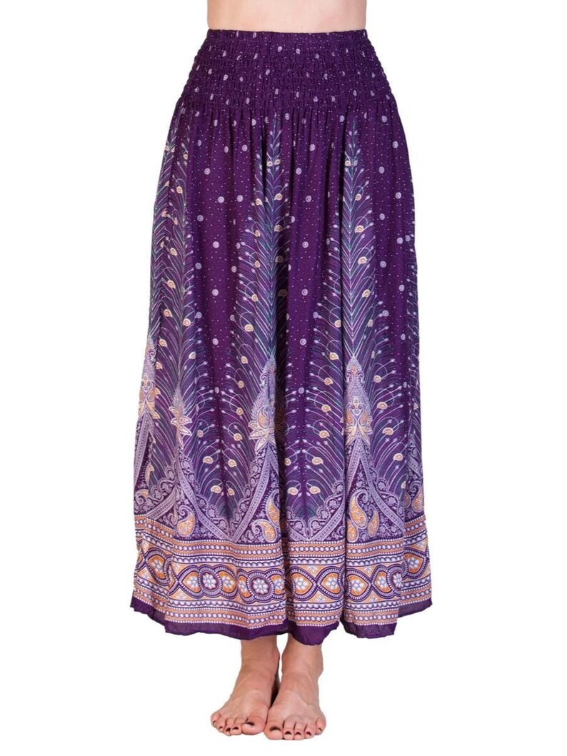 May include: A long, flowing skirt in shades of purple with a decorative peacock feather pattern. The skirt features an elastic waistband and a detailed border with paisley and floral designs. The fabric has a soft, flowing appearance.