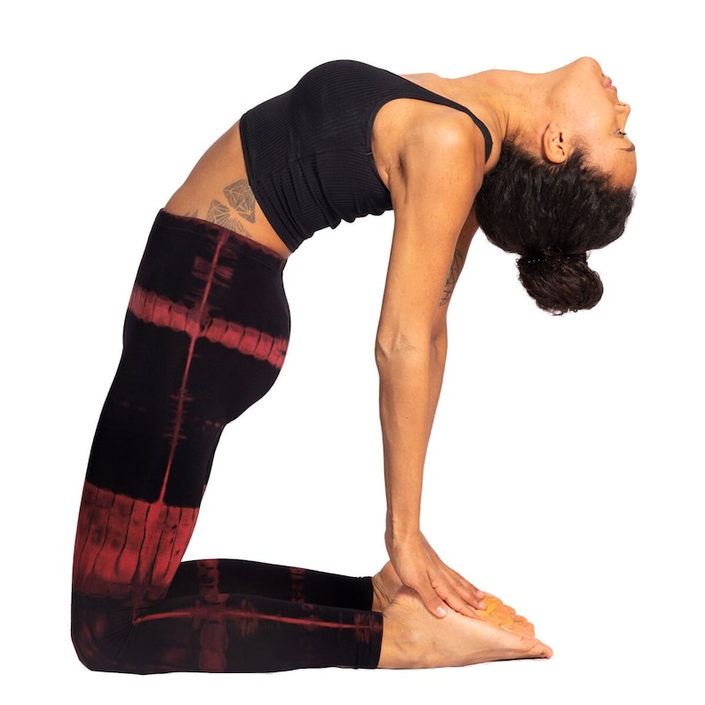 May include: A person in a yoga pose, wearing a black ribbed crop top and black leggings with a red tie-dye pattern. The person is bending backward, with arms extended and head tilted back. The background is white.