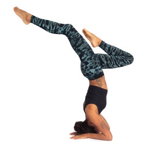 May include: Black yoga top and leggings with a teal tie-dye pattern. The leggings are full-length. The person is in a headstand pose, with legs extended. The background is white.