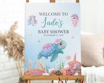 May include: Welcome to Jade's Baby Shower sign with a blue, pink, and green sea turtle with a flower crown, an octopus, and a seahorse. The sign is on a wooden easel and the date is November 31, 2022.