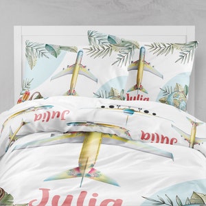 May include: White bedding set with a tropical theme featuring a yellow airplane with colorful floral details. The bedding set includes a duvet cover and two pillowcases. The name "Julia" is printed on the bedding in a pink font.