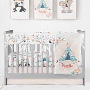 May include: A gray crib with a white and pink floral crib bedding set. The bedding features a pattern of animals, including a panda, a koala, and a fox. The crib also has a white bumper with a similar pattern. The blanket has a blue and white teepee design with the name "Amelia" written on it.