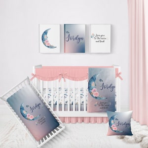 May include: A nursery room with a crib, a pink and blue blanket, and a pillow with a crescent moon and floral design. The pillow and blanket have the name "Jordyn" printed on them. The walls are decorated with three framed prints, one with a crescent moon and floral design, one with the name "Jordyn" and one with the text "Love you to the moon and back".