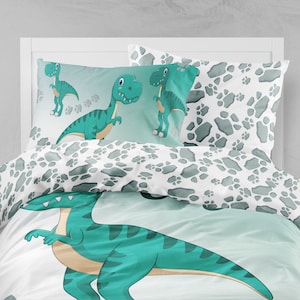 May include: A green dinosaur bedding set with a white background featuring a dinosaur footprint pattern. The set includes a duvet cover and two pillowcases.